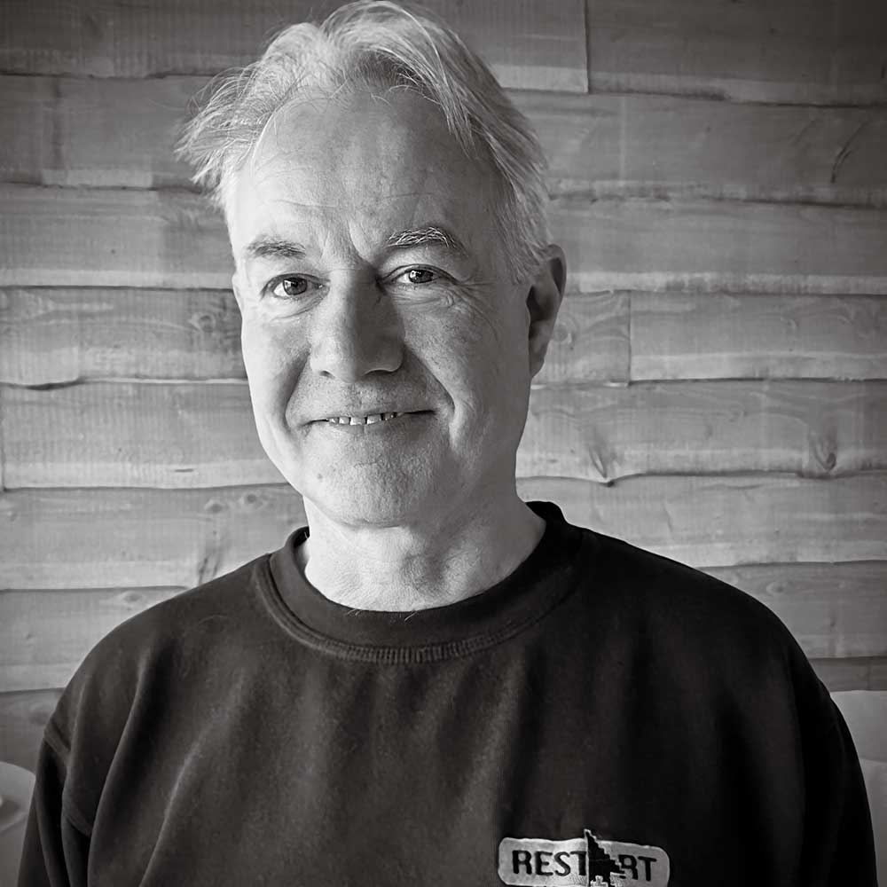 nigel-entwistle black and white portrait image of smiling man with grey hair and black sweater